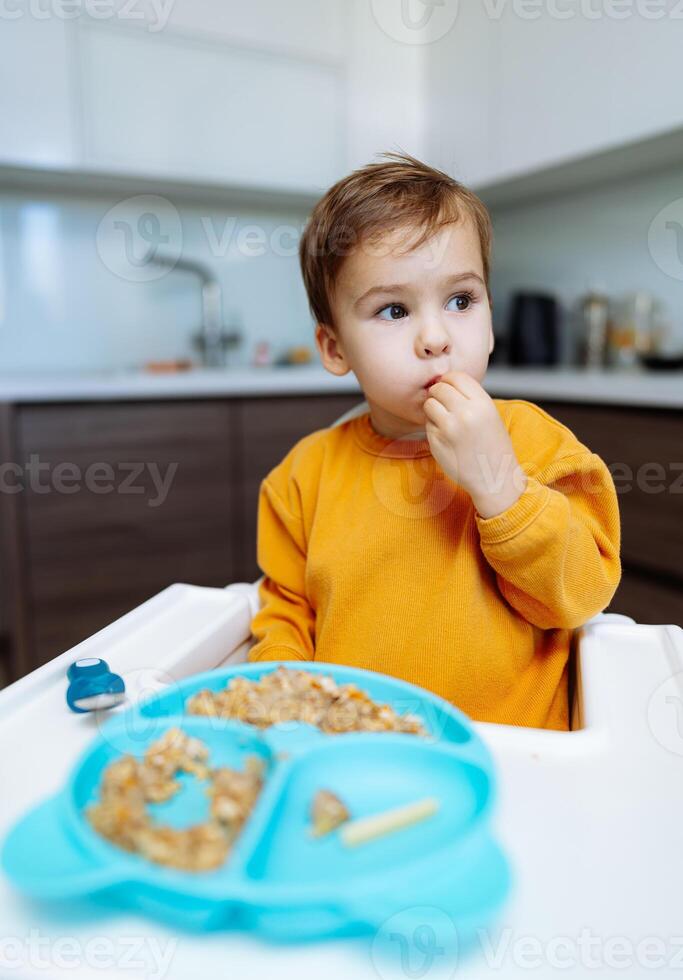 A Young Boy Enjoying a Bowl of Cereal. A young boy sitting at a table eating cereal photo