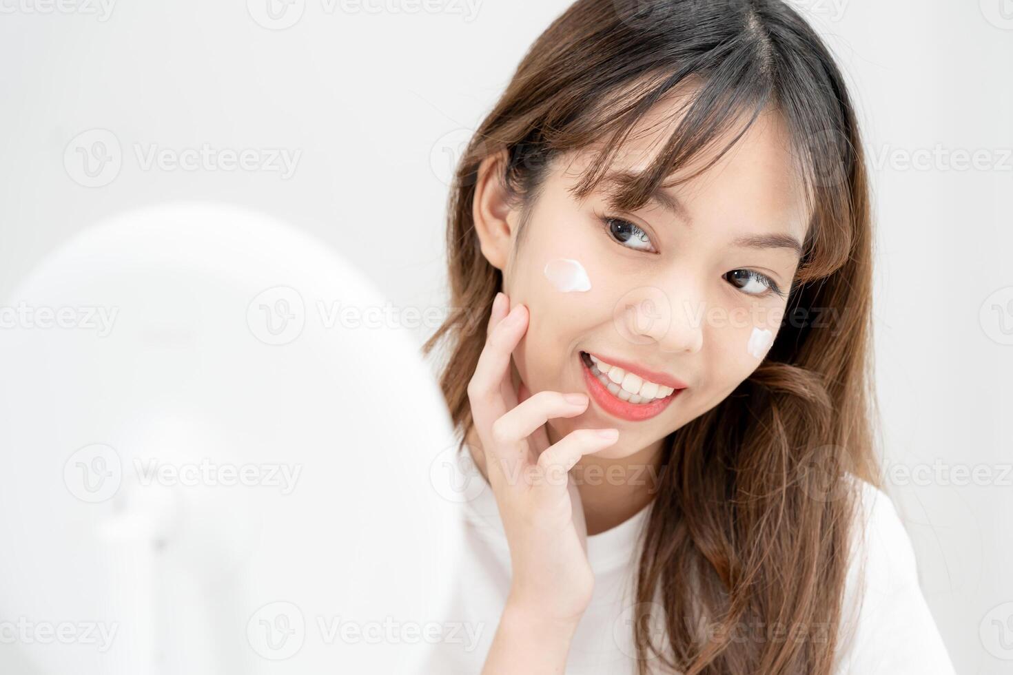 Beautiful Asian woman sit in front of a mirror. face of a healthy woman applying cream and makeup. Advertisement for skin cream, anti-wrinkle, baby face, whitening, moisturizer, tighten pores serum photo