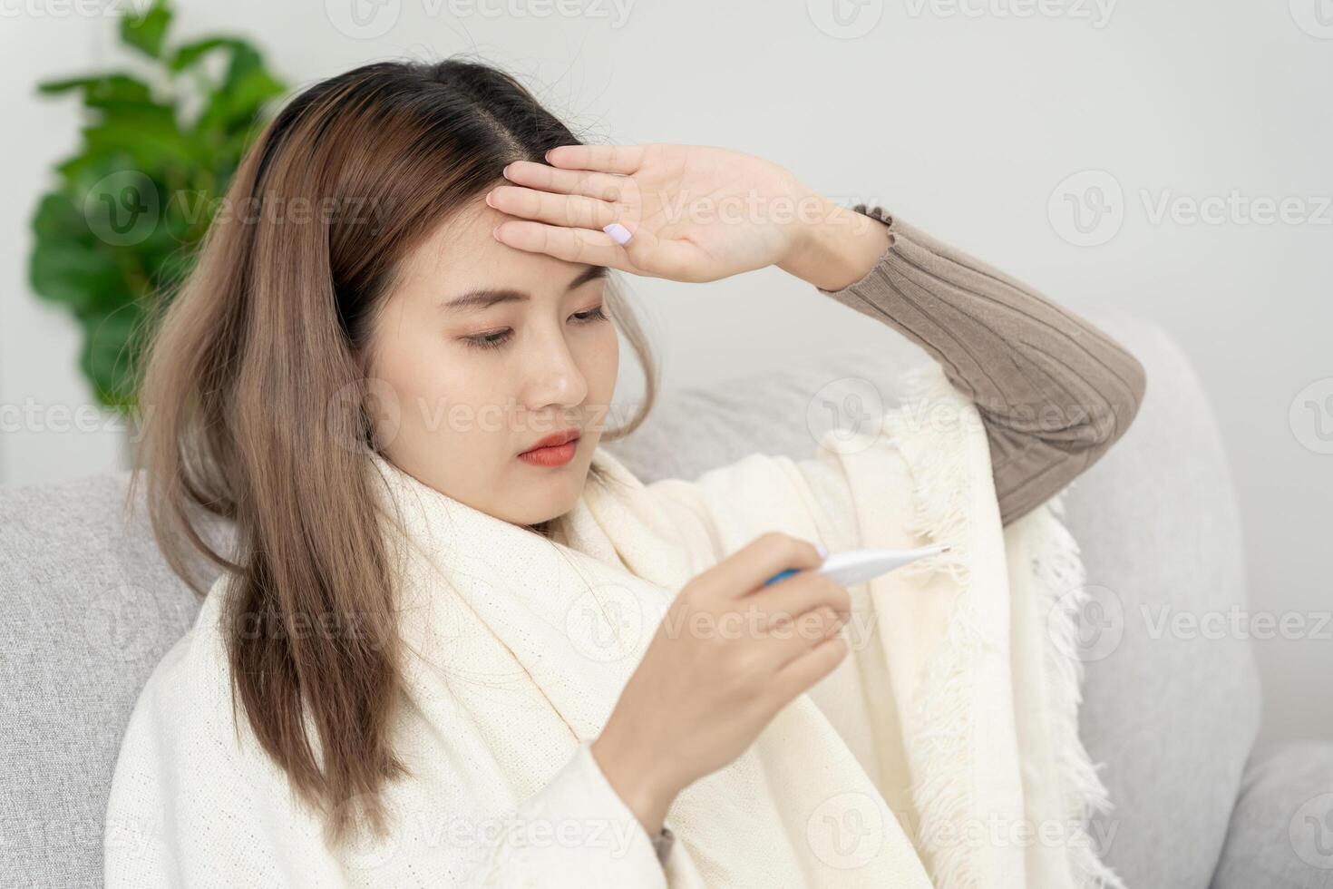 Young Asian woman having high fever while checking body temperature, female sneezing and runny nose with seasonal influenza, allergic, digital thermometer, virus, coronavirus, illness, respiratory photo