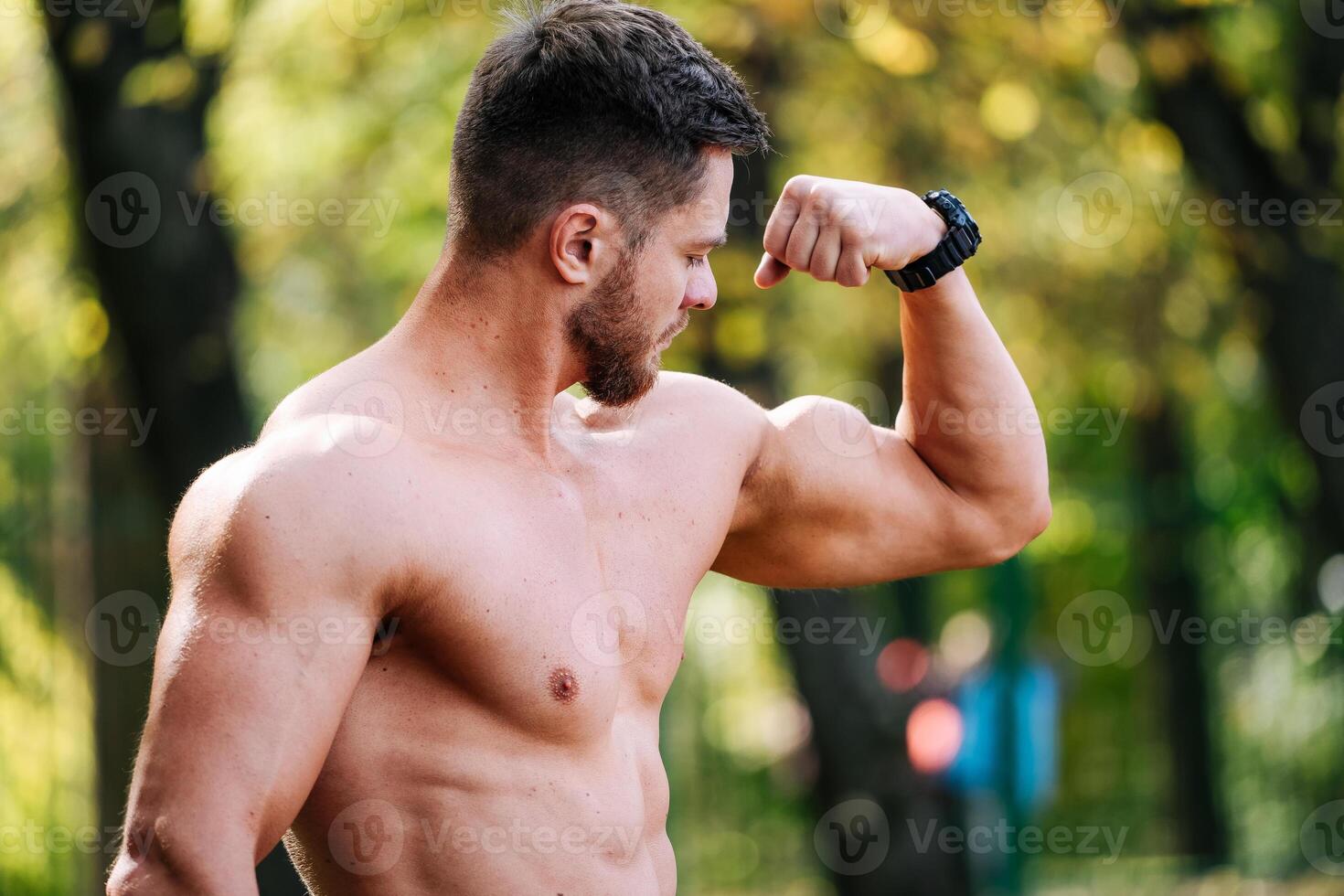 un fuerte hombre demostrando su músculos. un sin camisa hombre flexionando su músculos en un parque foto