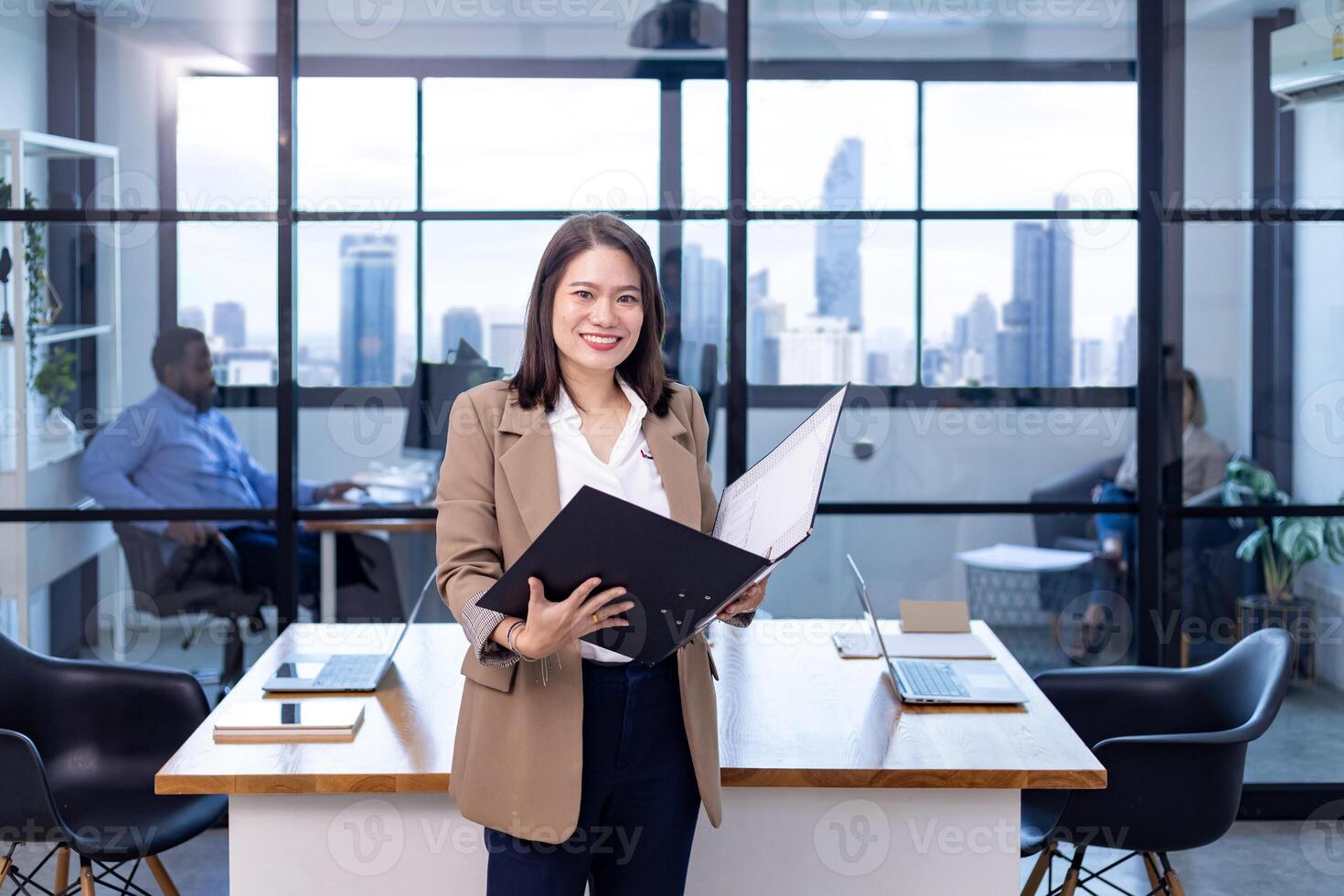retrato de asiático negocio CEO mujer es en pie en el oficina a el mesa con documento archivo y demostración estadística gráfico demostración anual reporte y rascacielos antecedentes foto