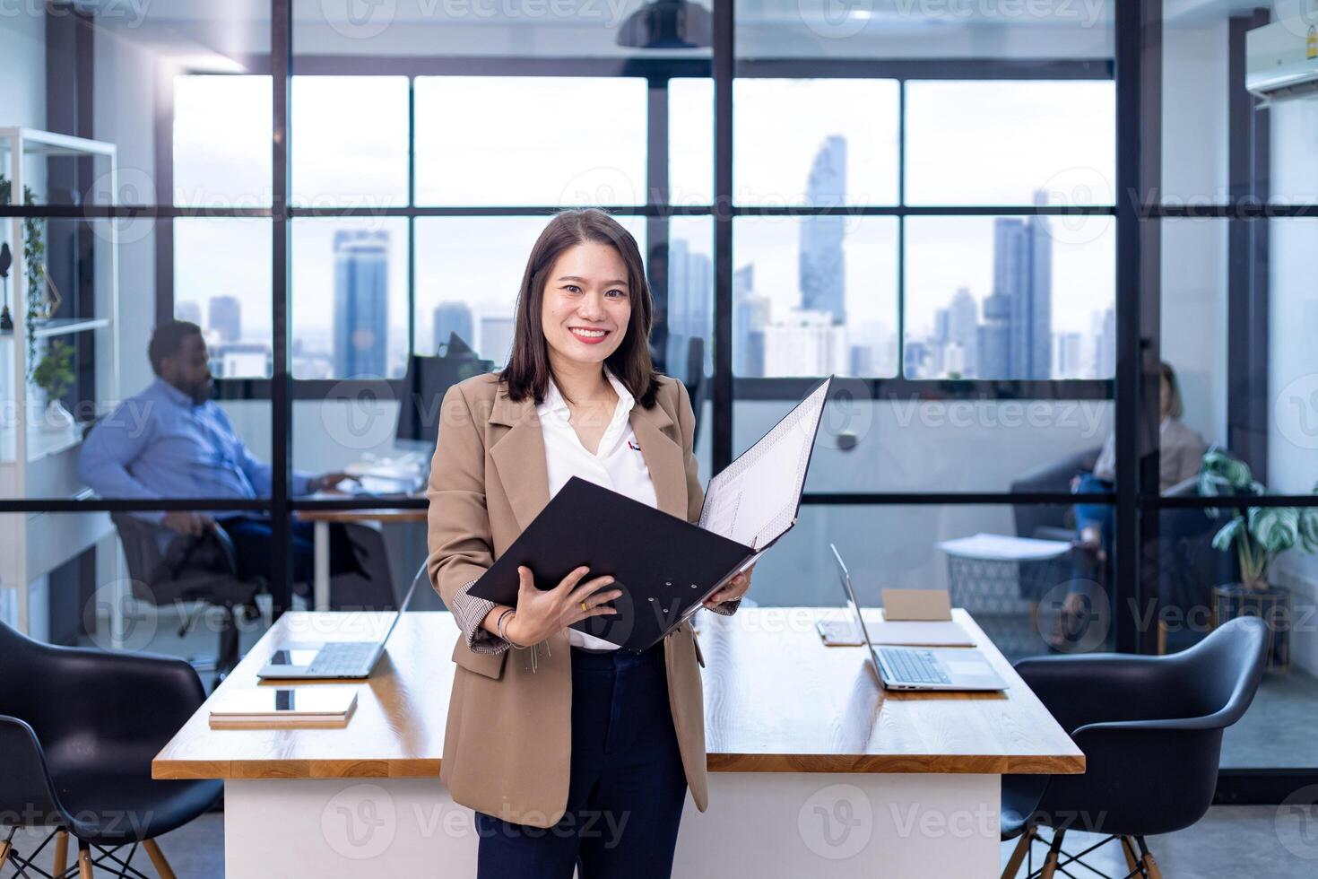 Portrait of Asian business CEO woman is standing in the office at the table with document file and showing statistic chart showing annual report and skyscraper background photo