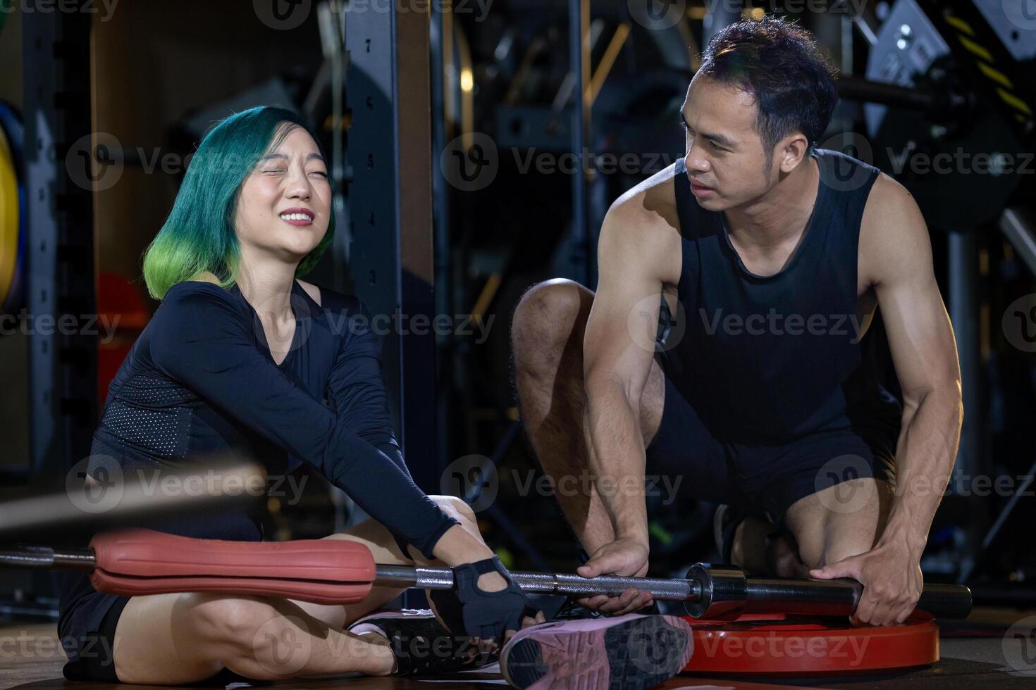 Asian woman got accident in the gym after weight training workout with her trainer rush to help on dark background for exercising and fitness photo