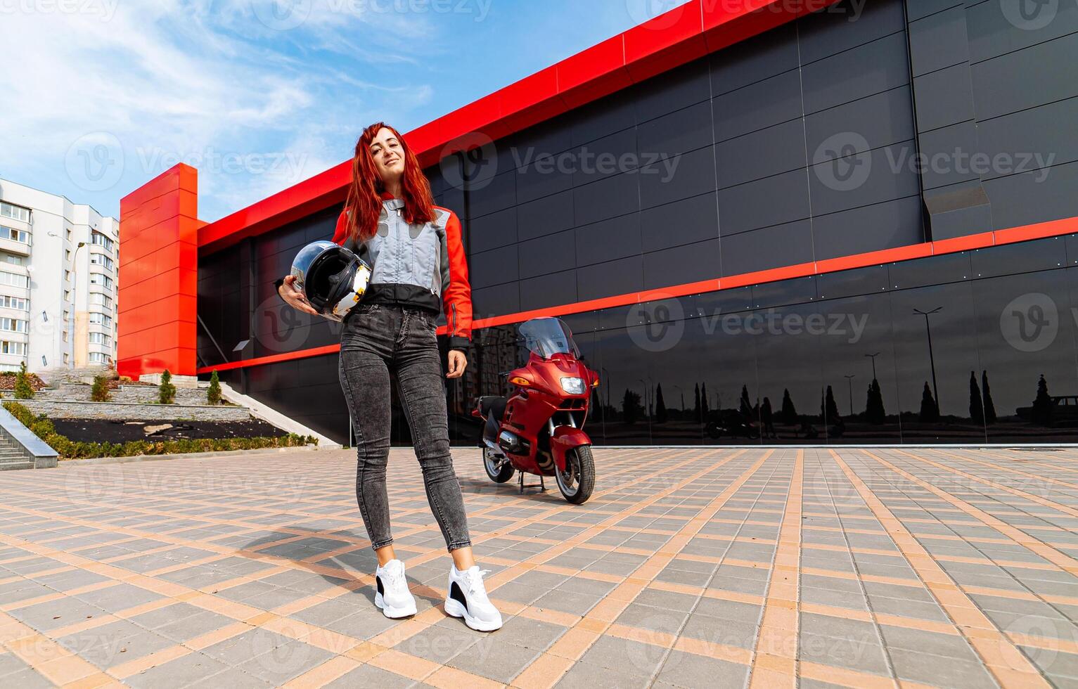 The Adventurous Woman and Her Bold Red Motorcycle. A woman standing in front of a red motorcycle photo