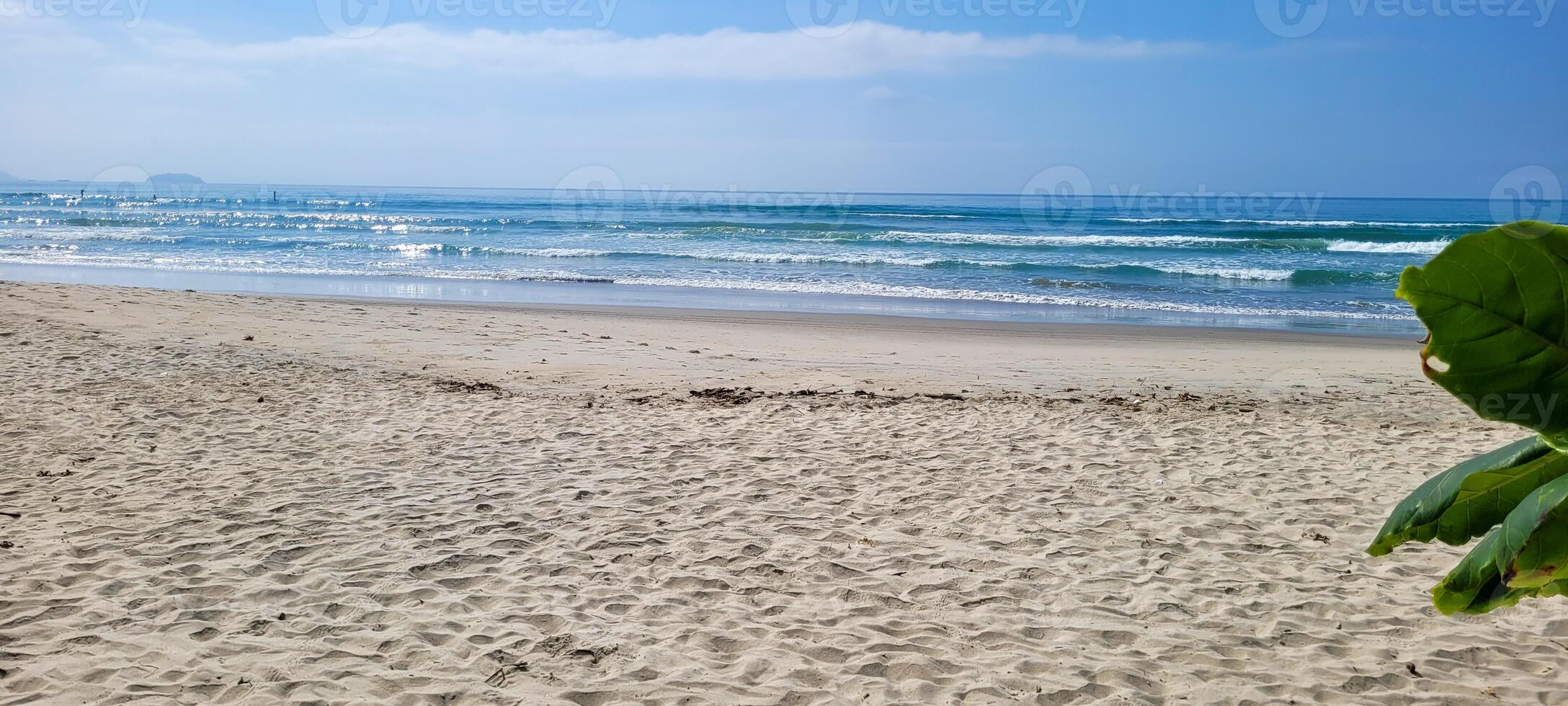 image of beach with white sand and calm sea on sunny day with bathers and surfers on the beach photo