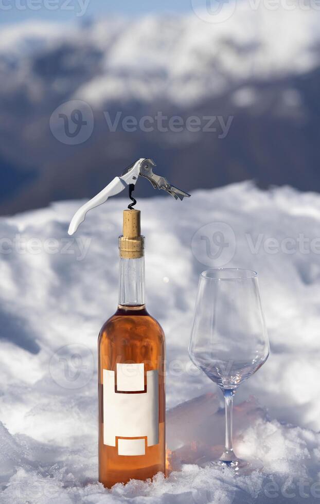 un botella de vino y un vaso de vino sentado en un nieve cubierto superficie foto