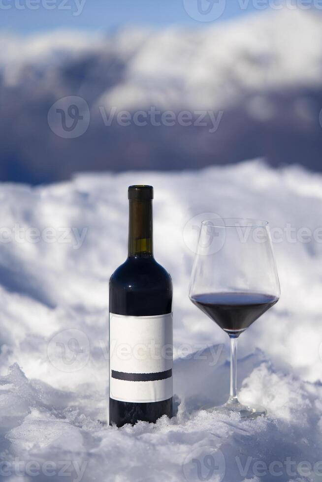 a bottle of wine and a glass of wine on a snowy mountain photo