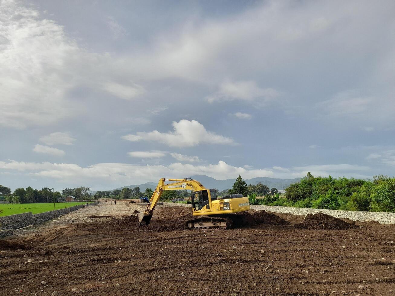 West Lombok Regency, Indonesia - February 4, 2024. Outdoors, a Backhoe is at work leveling the ground for a housing site, with a blue sky in the background. photo