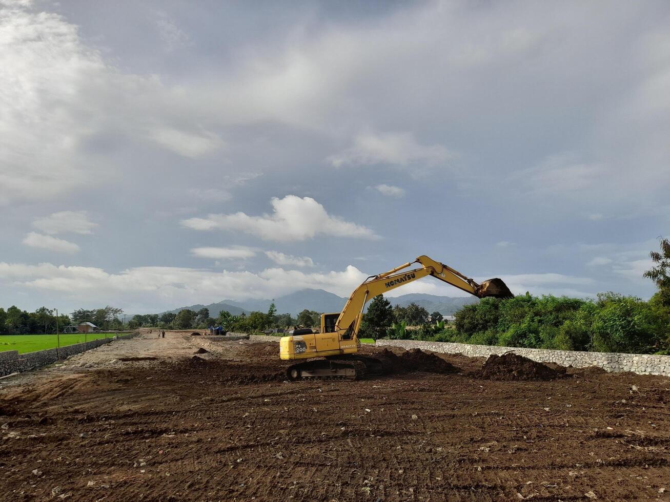 West Lombok Regency, Indonesia - February 4, 2024. Outdoors, a Backhoe is at work leveling the ground for a housing site, with a blue sky in the background. photo