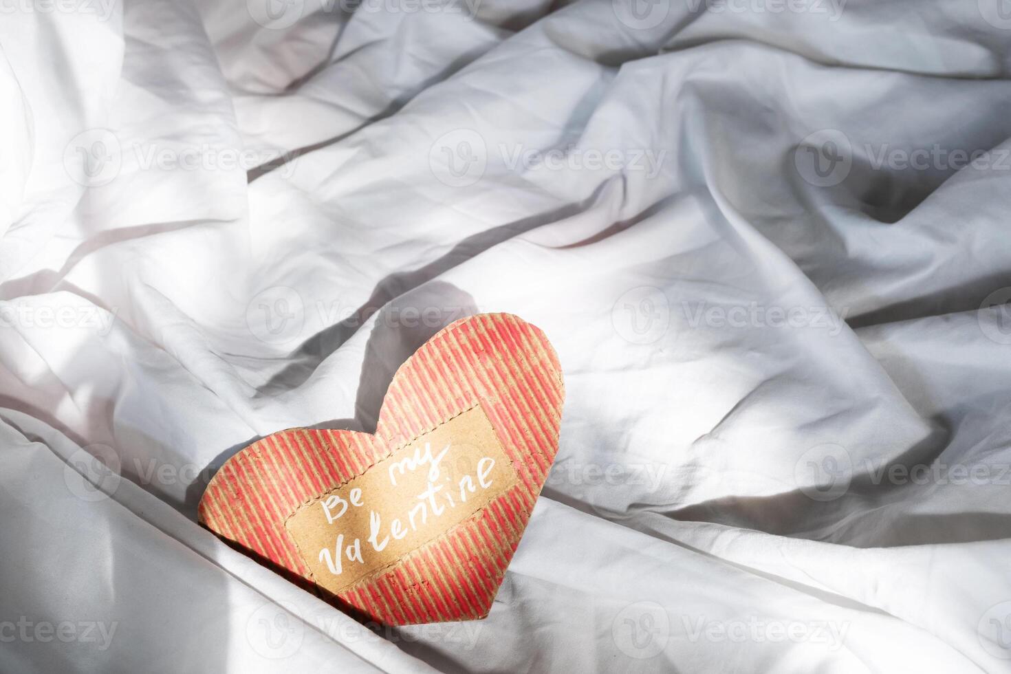 Handmade heart shaped Valentine card on rumpled bedding. photo