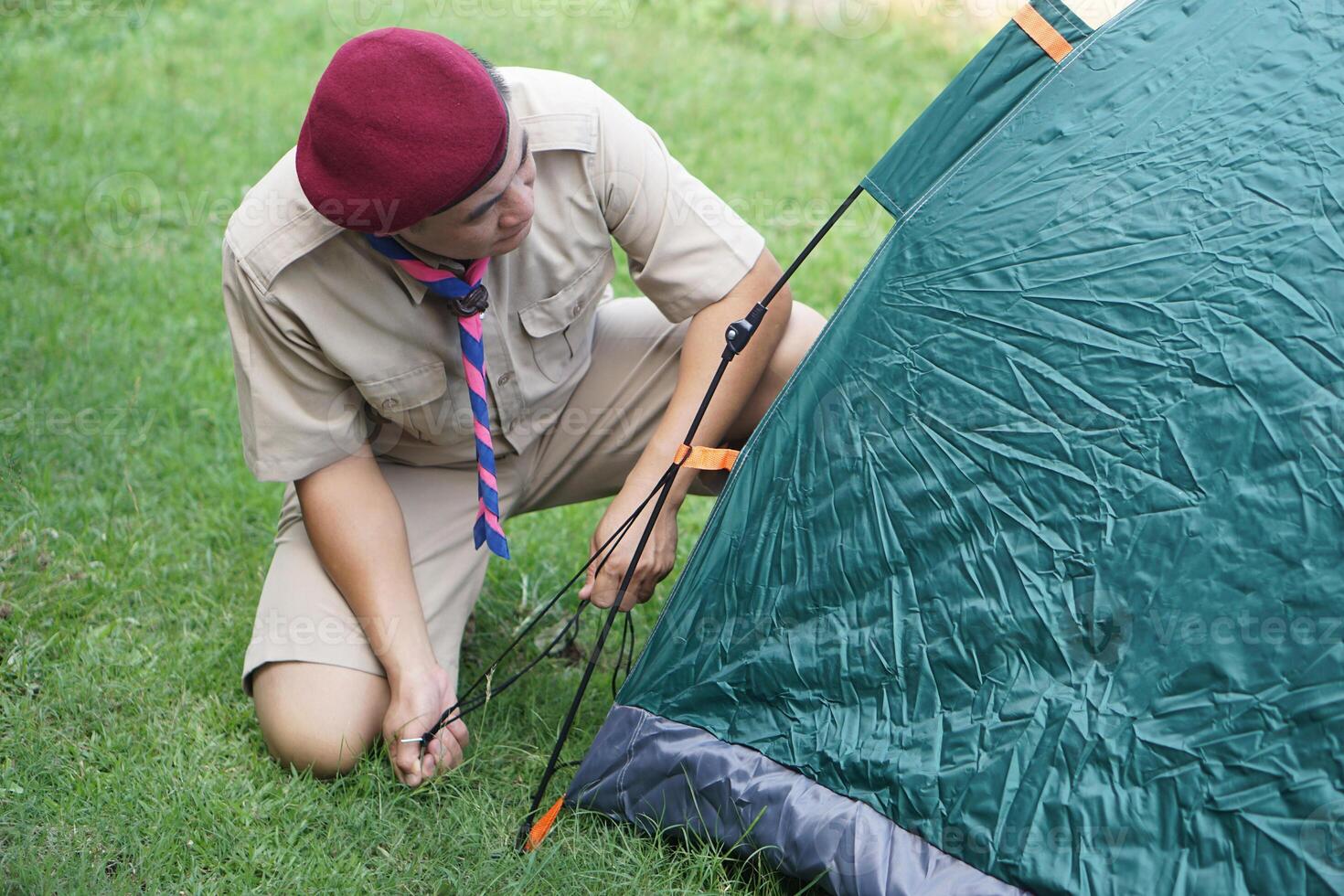 Thai boy scout is setting up the tent at campsite for camping outdoor. Concept, pitching camping tent, accomodation for temporary outdoor sleeping as scout hiking activity. photo