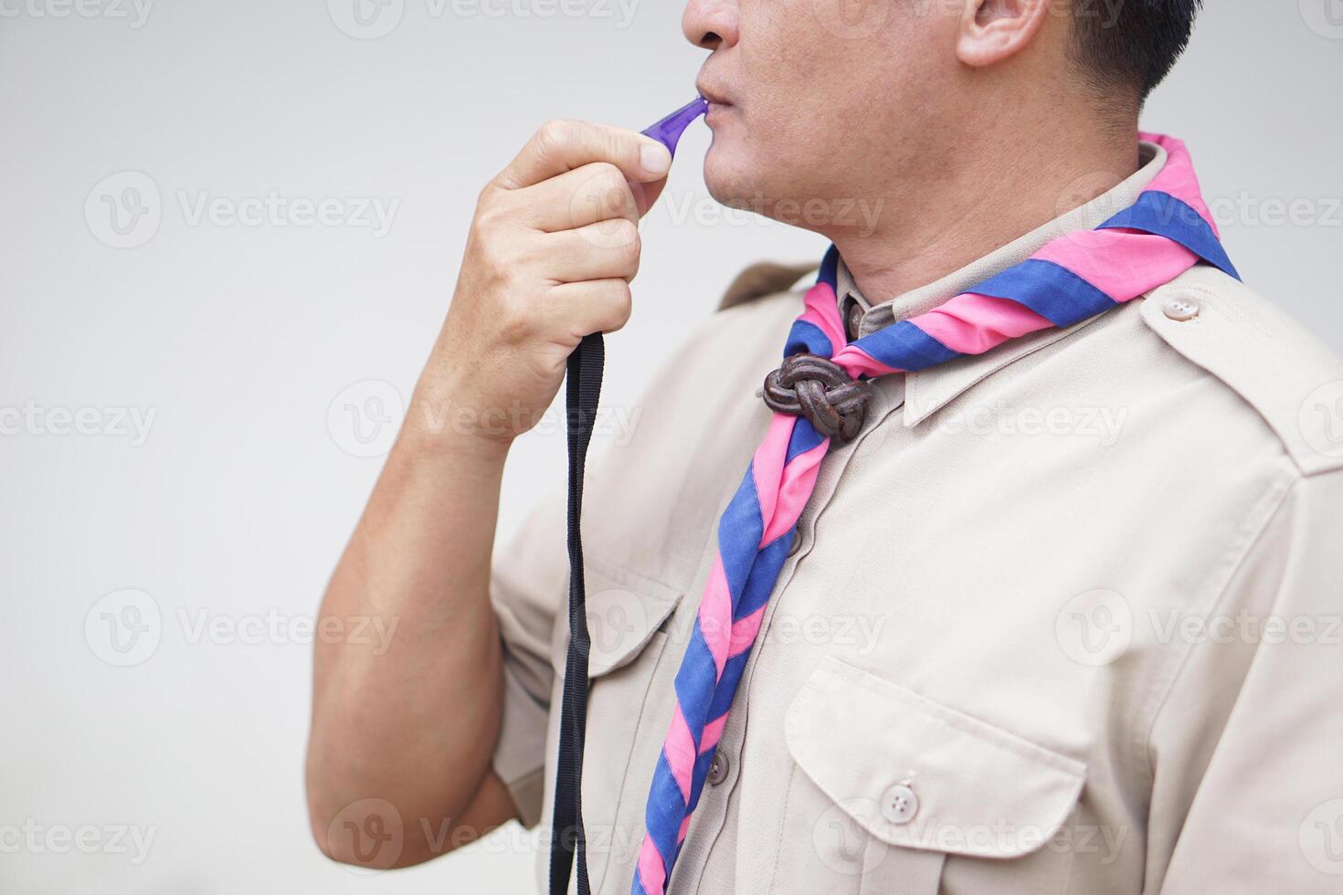 Close up man wears boy scout uniform is blowing the whistle. Concept, Scout blow whistle as meaningful sign for doing activity to assembly, start competition or playing games in scout lesson. photo