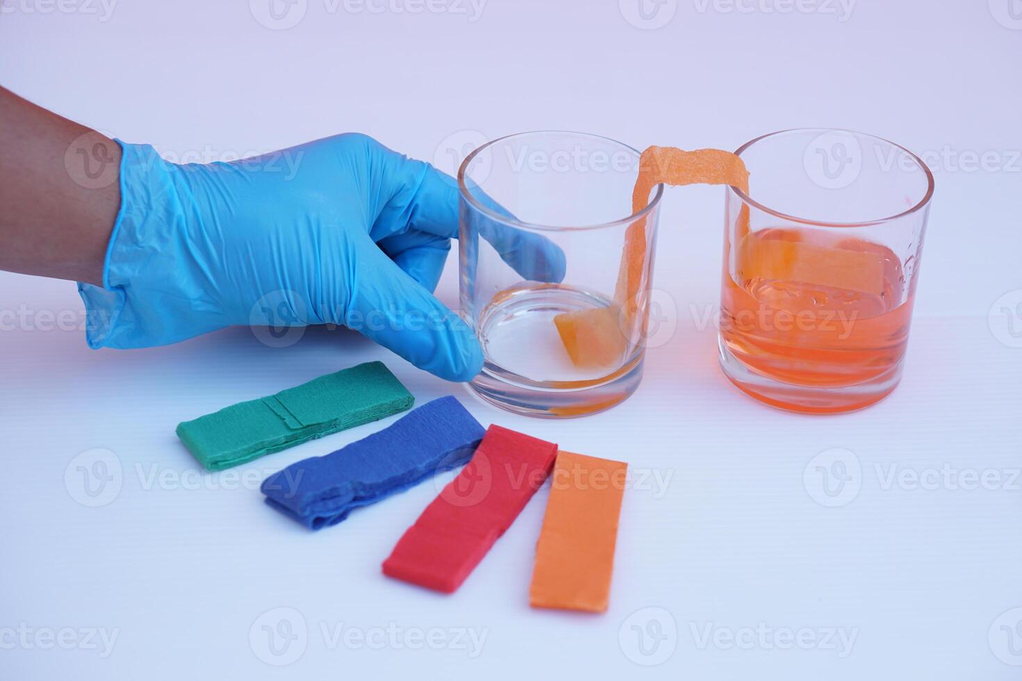Hand wear blue glove, hold glass of color paper strip to absorb water to another glass. Concept, science lesson activity. Easy experiment for learning. Teaching education materials.  Learning design photo