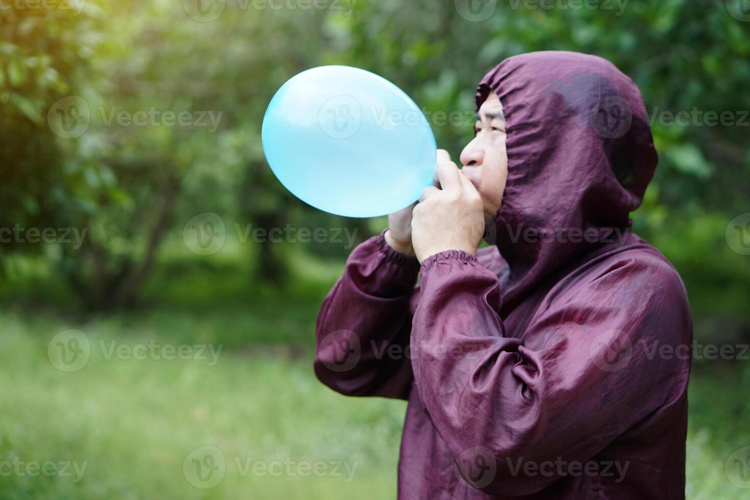 Asian man is blowing, inflating air into a balloon in the park. Concept, prepare balloon for playing games as a toy, decorate party or celebration. Recreation or leisure activity. Fun and happy time. photo