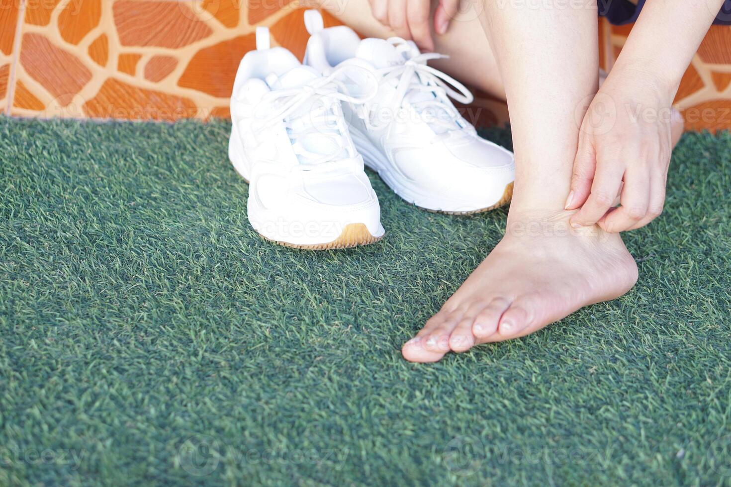 Close up woman hand is scratching her itchy feet. Concept, health problems, skin allergy, rashes, insect bite, fungus or dermatitis on feet from wearing unhygienic and humid shoes. photo