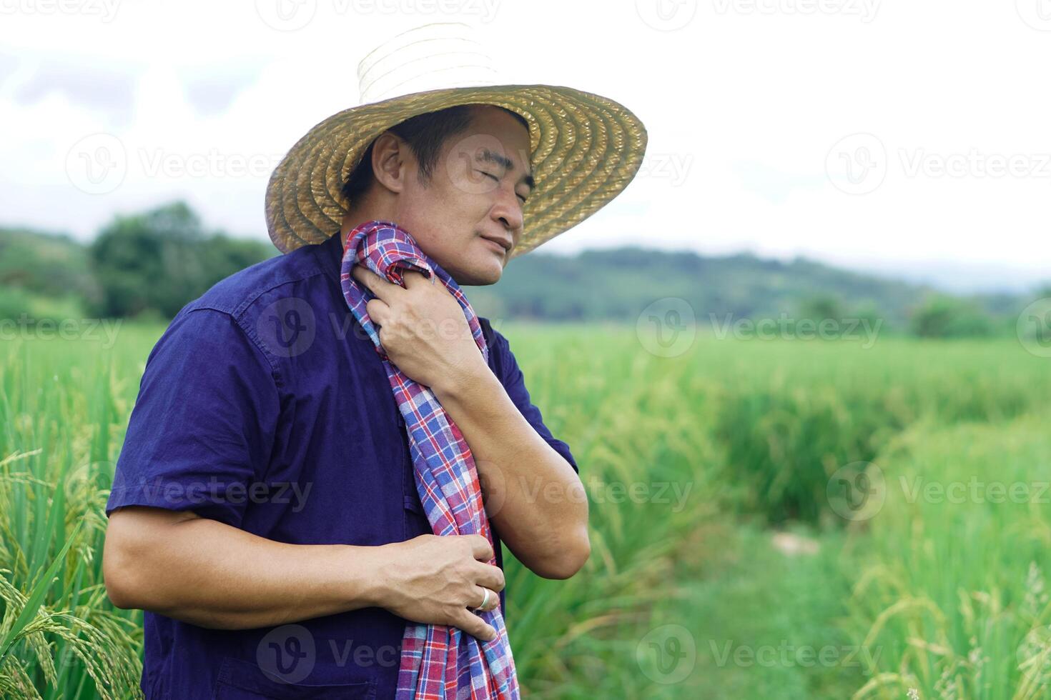 Asian man farmer is at paddy field, feels tired and hot, use Thai loincloth to wipe his face. Concept, Agriculture occupation,  Farmer work hard against poverty. Lifestyle of farmer. photo