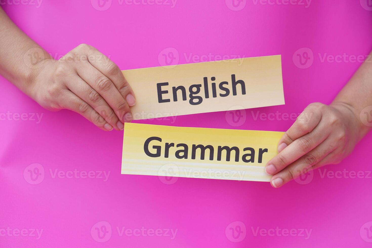 Close up hands hold  word card paper with text English grammar. Pink background. Concept, English language grammar teaching. Using word card to create for playing educational fun games or practice photo