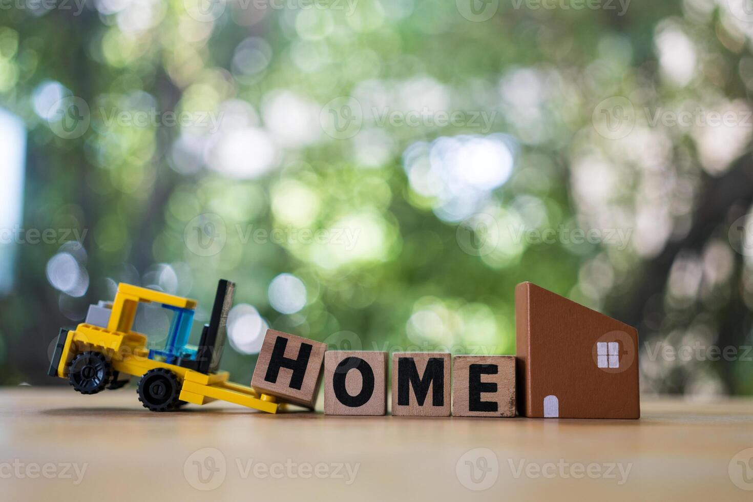 Forklift truck carries a the letter H to complete HOME near mini model home against nature background photo