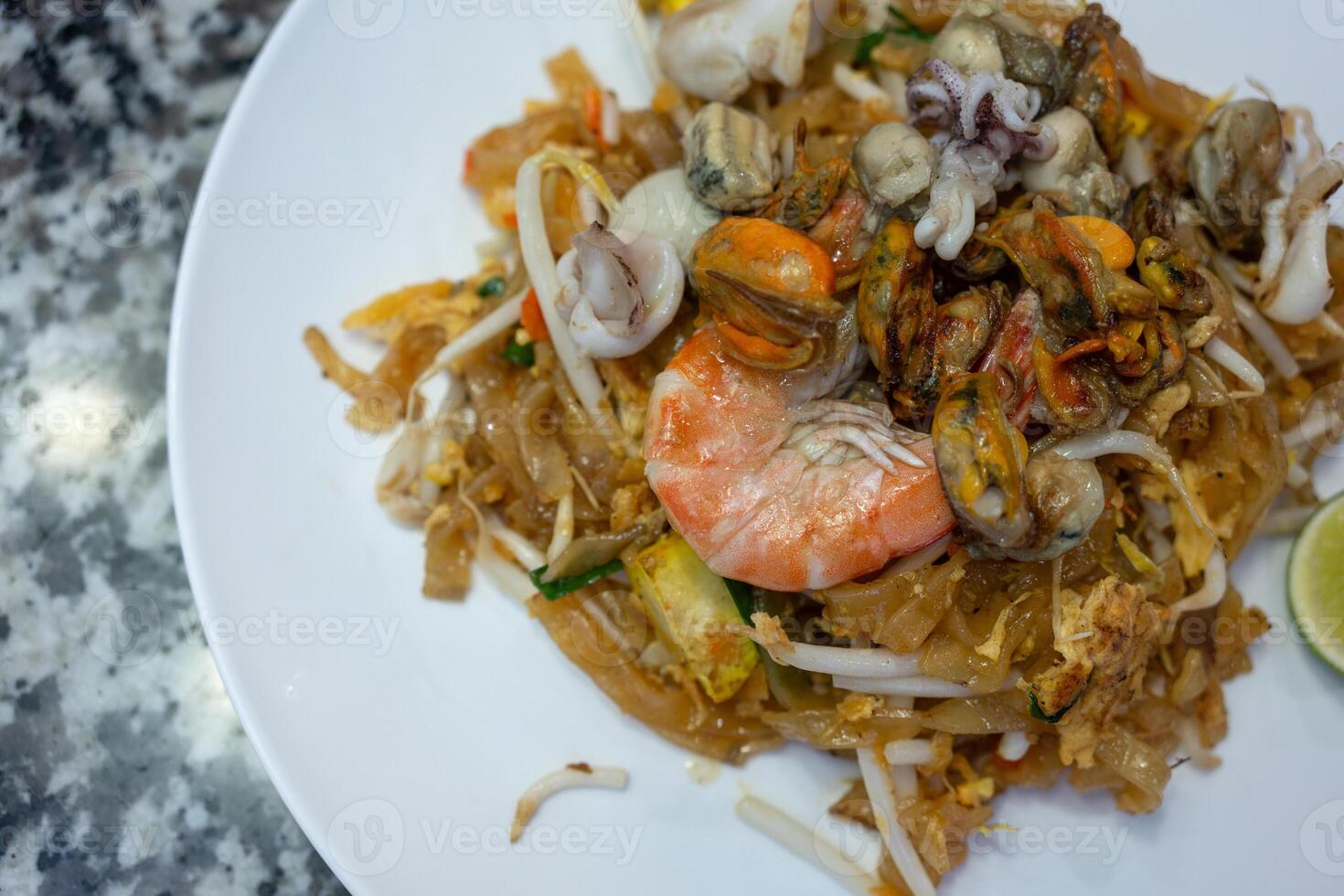 Pat Thai, thin rice noodles fried with tofu, vegetables, egg and many seafood on a white plate. photo