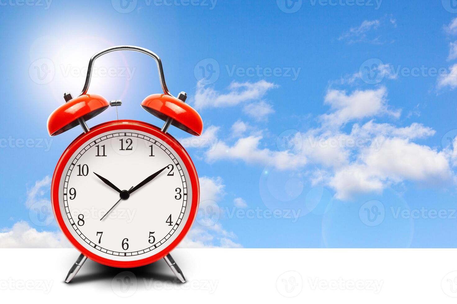 Red alarm clock on blue sky background photo