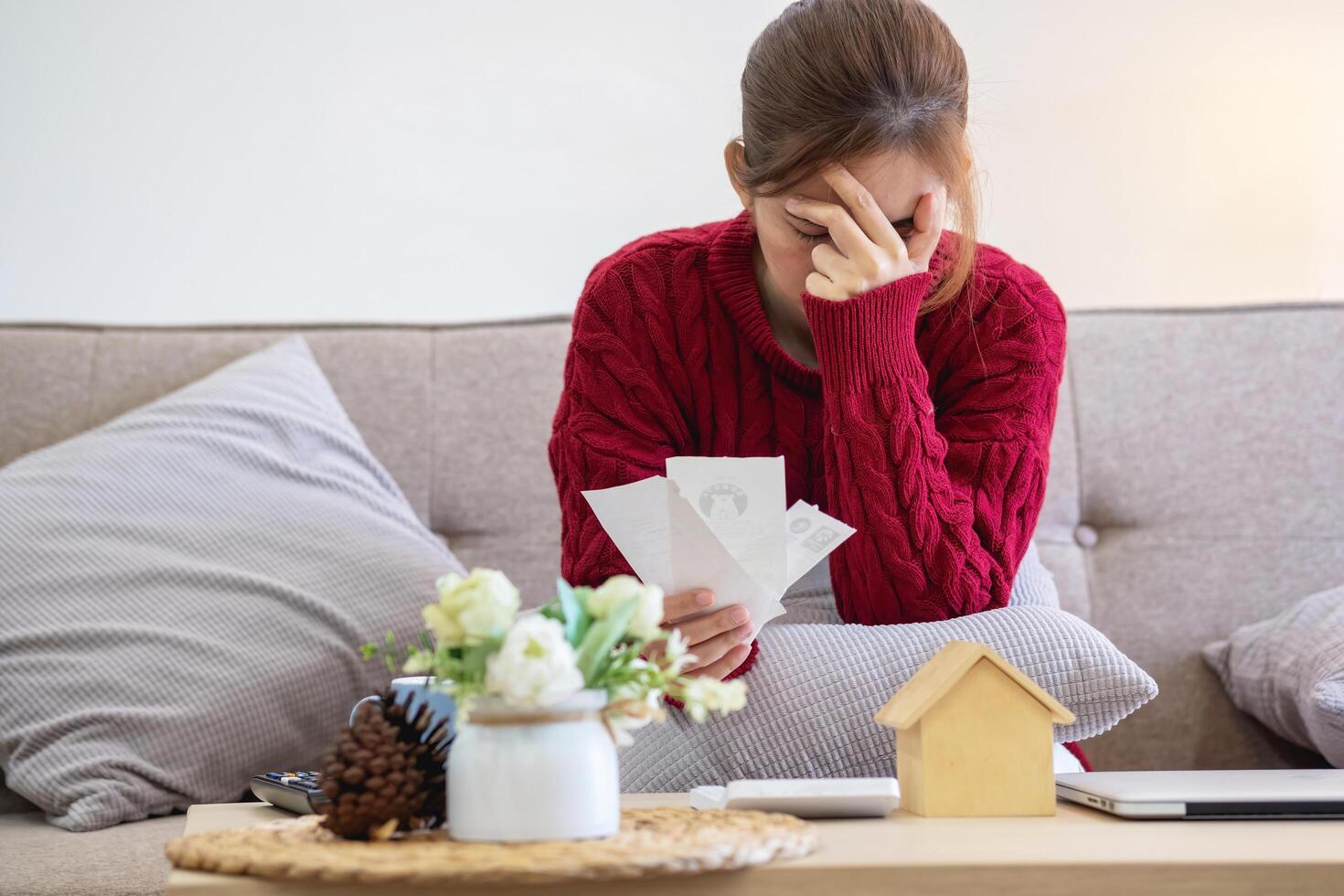 A young Asian woman sits on a sofa in her home, feeling worried and frustrated about her monthly expenses. Various utility bills. photo