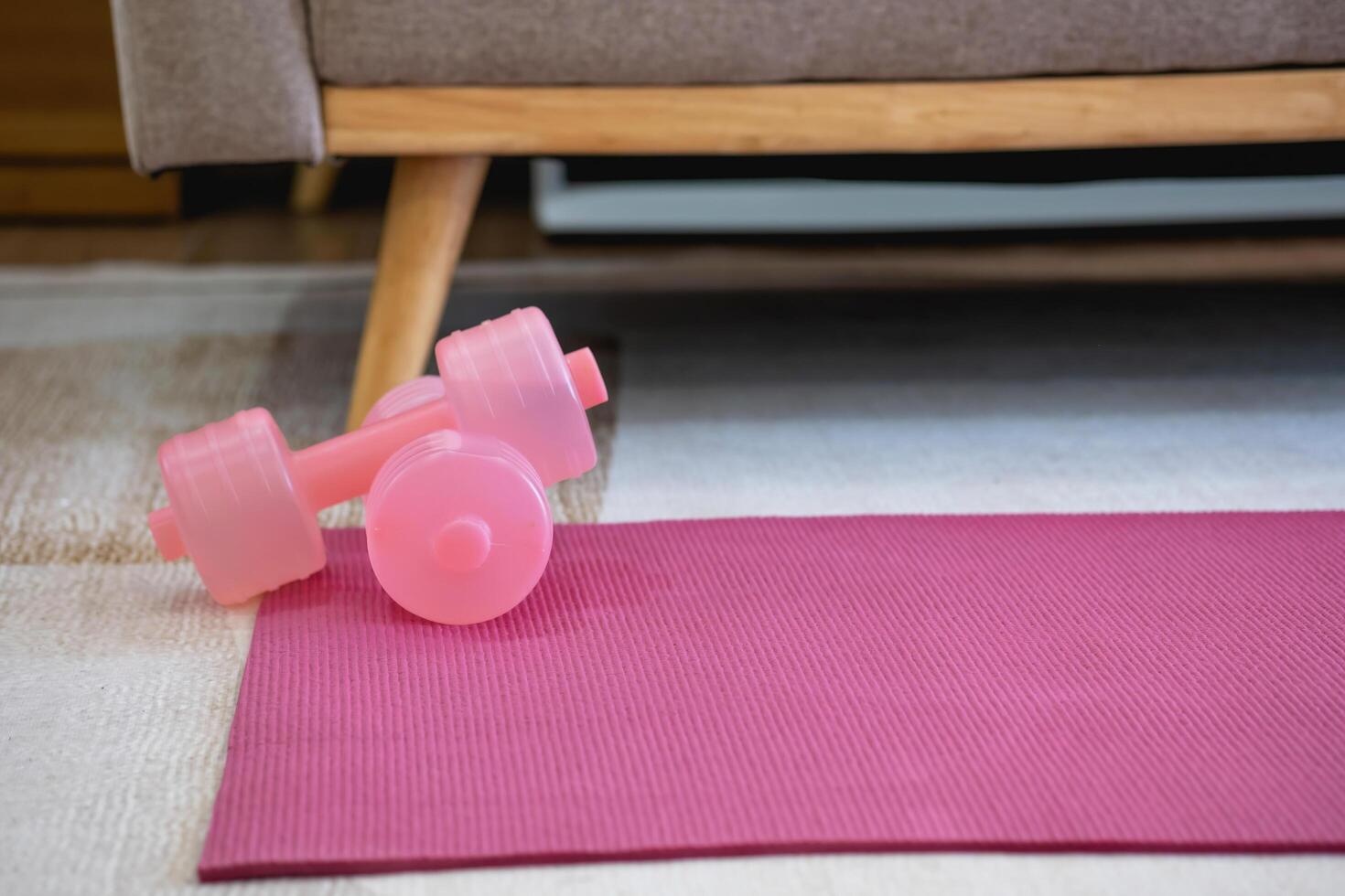 A pink yoga mat with two pink colored dumbbells on it. Fitness equipment for home exercise and flexibility training. photo