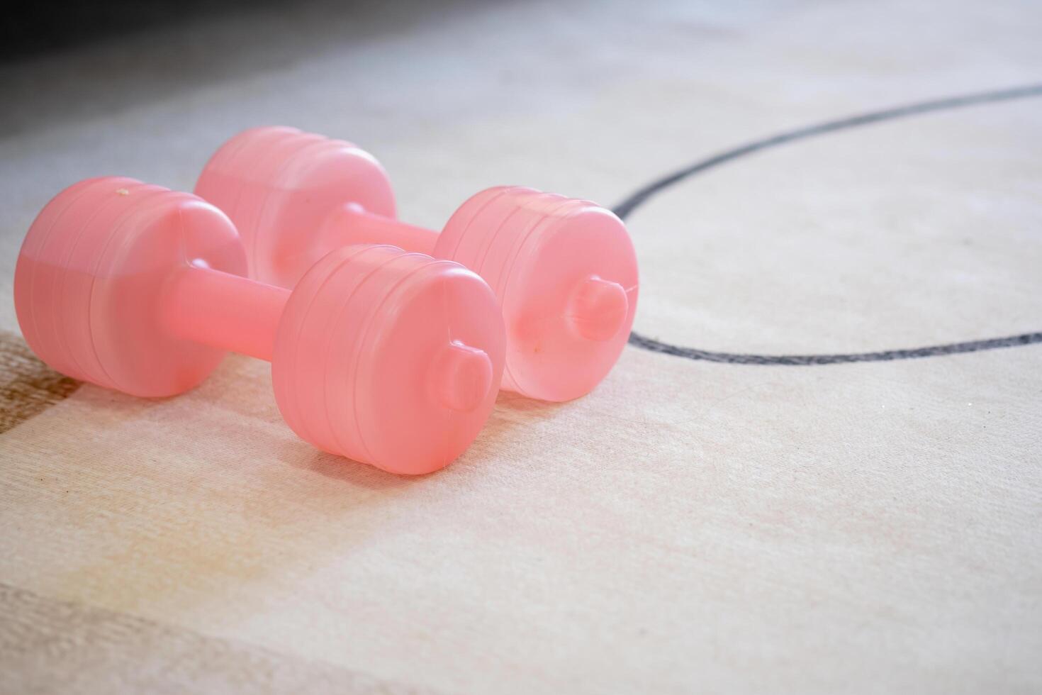 A pink yoga mat with two pink colored dumbbells on it. Fitness equipment for home exercise and flexibility training. photo