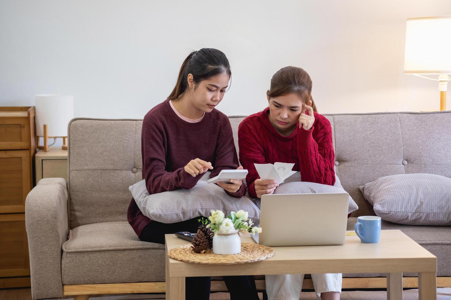 A young Asian woman sits on a sofa in her home, feeling worried and frustrated about her monthly expenses. Various utility bills. photo