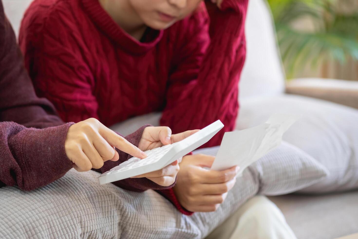 A young Asian woman sits on a sofa in her home, feeling worried and frustrated about her monthly expenses. Various utility bills. photo