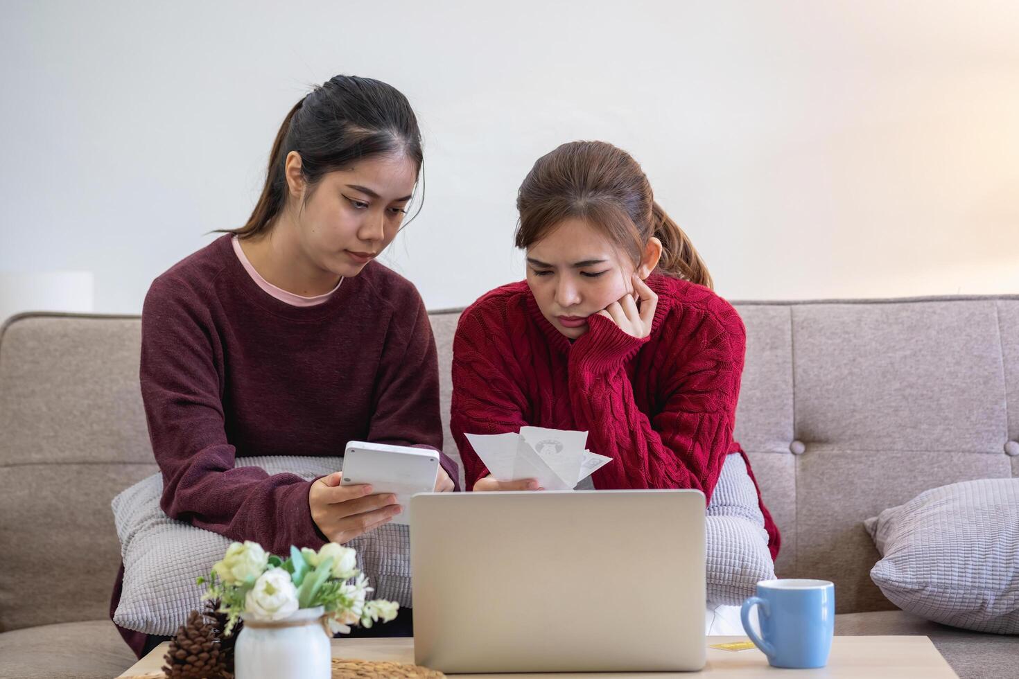 A young Asian woman sits on a sofa in her home, feeling worried and frustrated about her monthly expenses. Various utility bills. photo