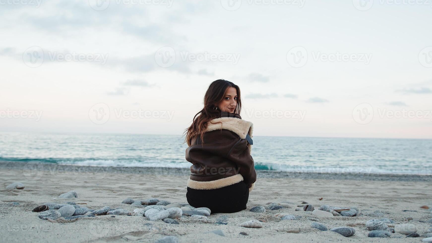 Girl seated on the beach near the ocean in overcast winter day photo