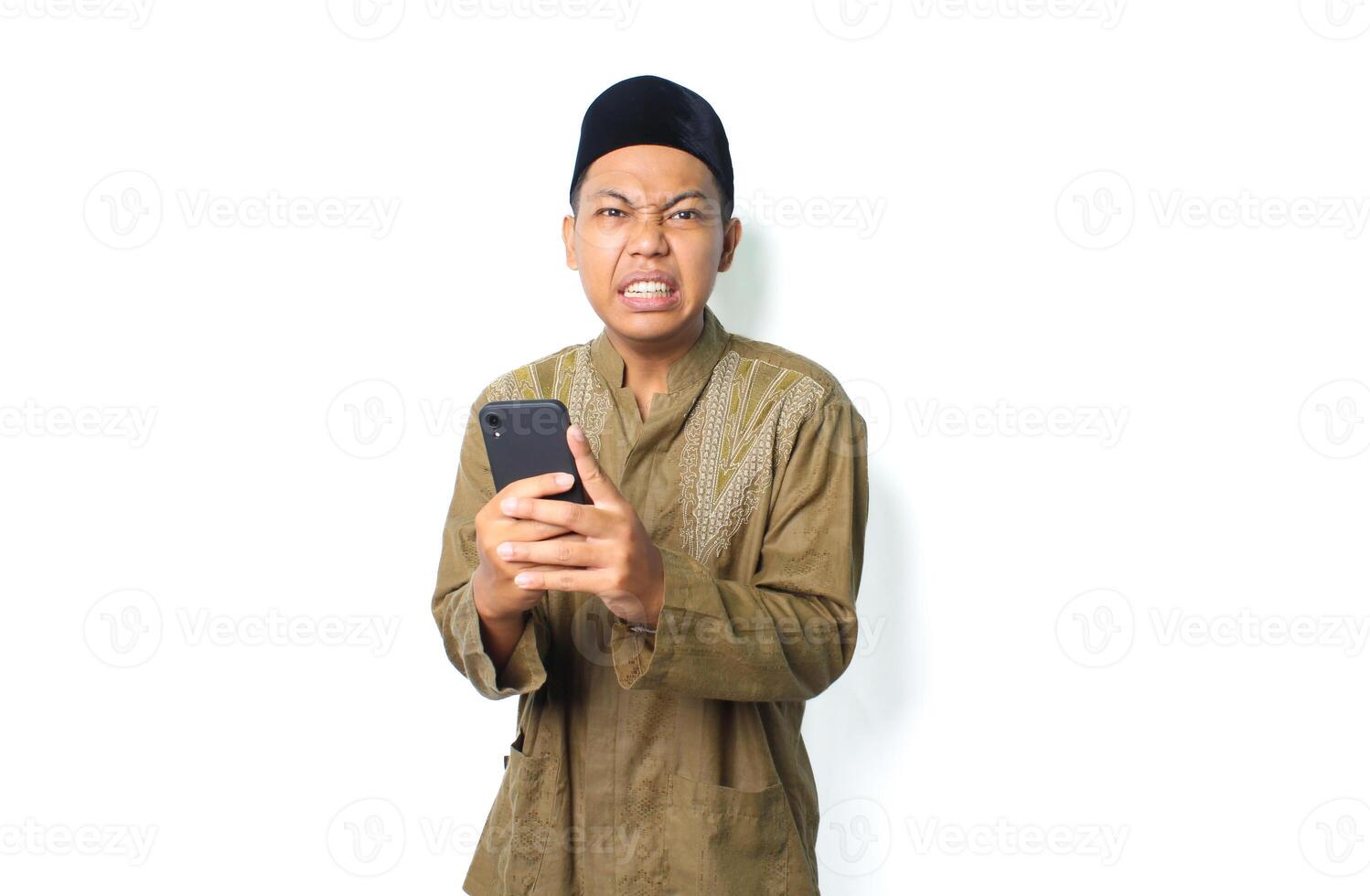 angry asian muslim man wearing islamic dress holding mobile phone isolated on white background photo