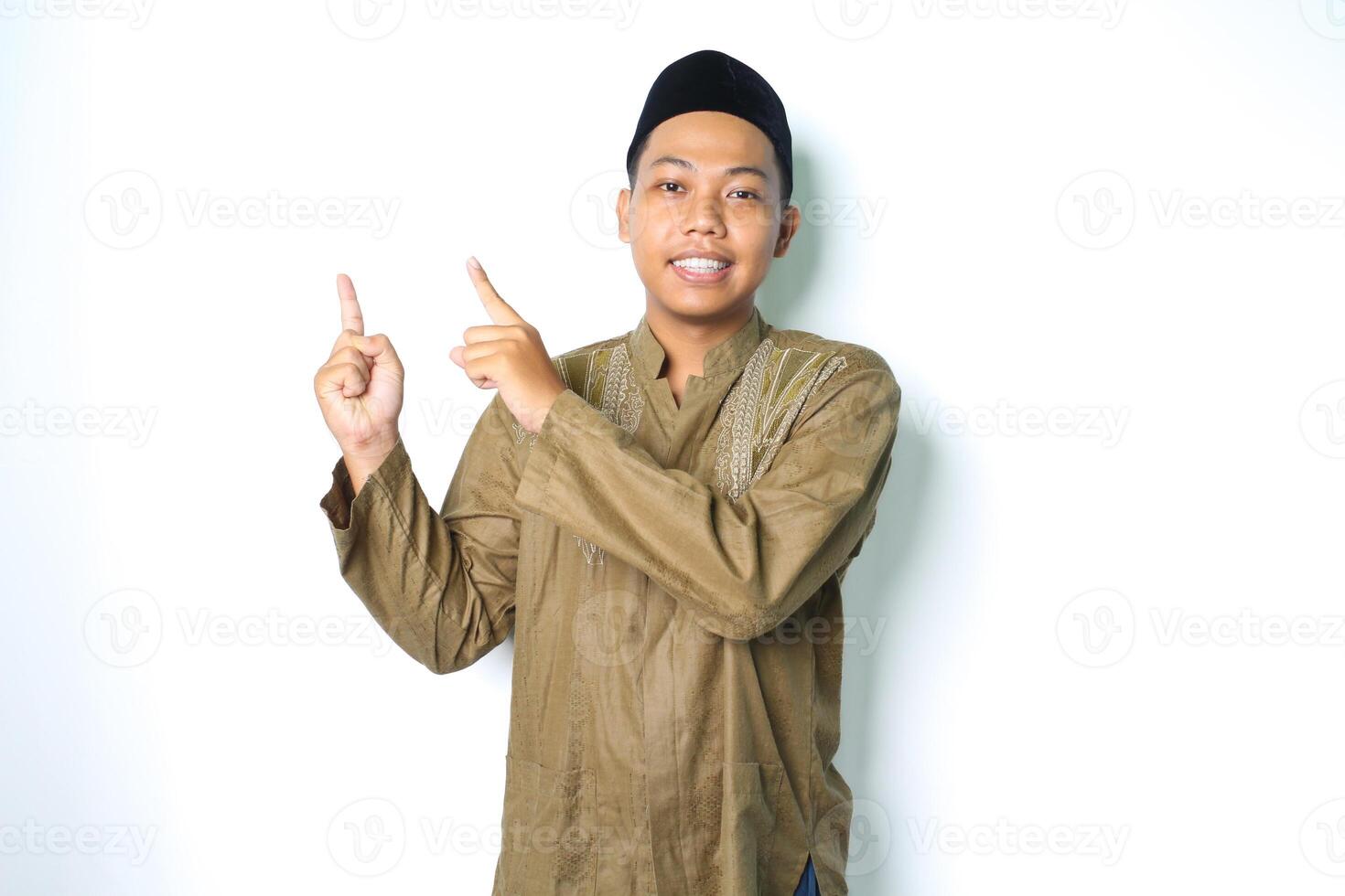 asiático musulmán hombre señalando a encima y sonriente a cámara vistiendo islámico vestir aislado en blanco antecedentes foto