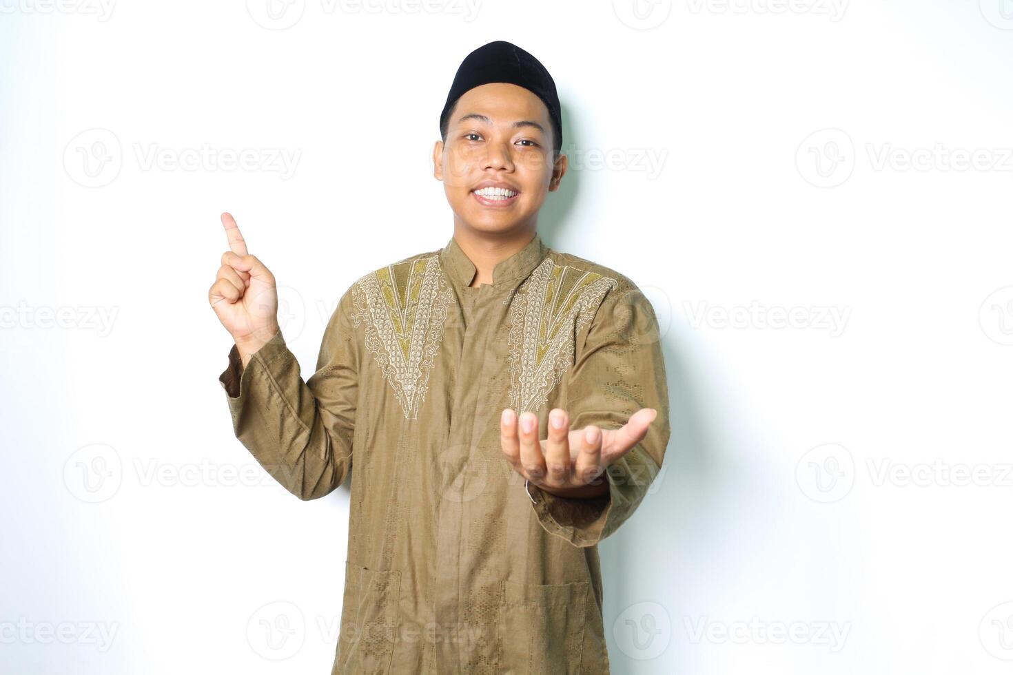 sonriente asiático musulmán hombre señalando a encima y presentación abierto palma a cámara vistiendo islámico vestir aislado en blanco antecedentes foto