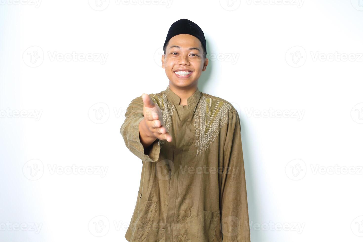 friendly smiling asian muslim man stretching hand at camera to offer handshake for forgiveness in eid mubarak celebration isolated on white background photo