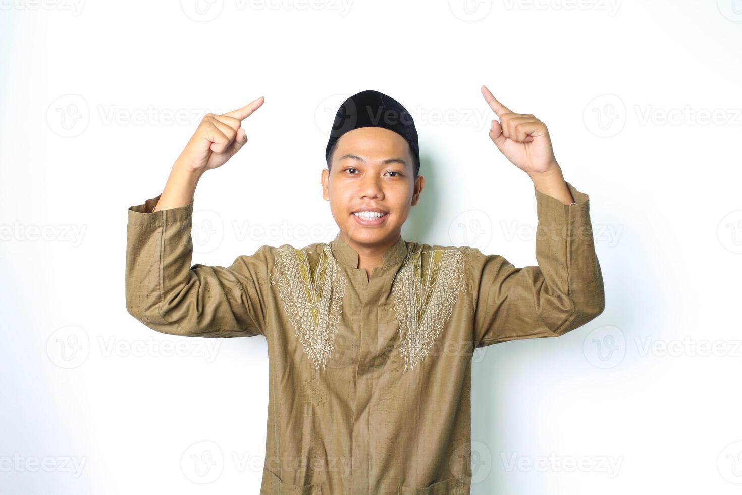 asian muslim man pointing to above and smiling at camera wearing islamic dress isolated on white background photo