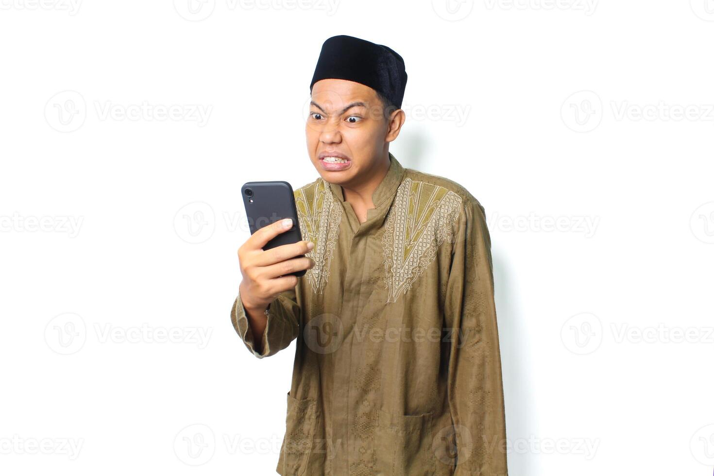 angry asian muslim man wearing islamic dress holding mobile phone isolated on white background photo