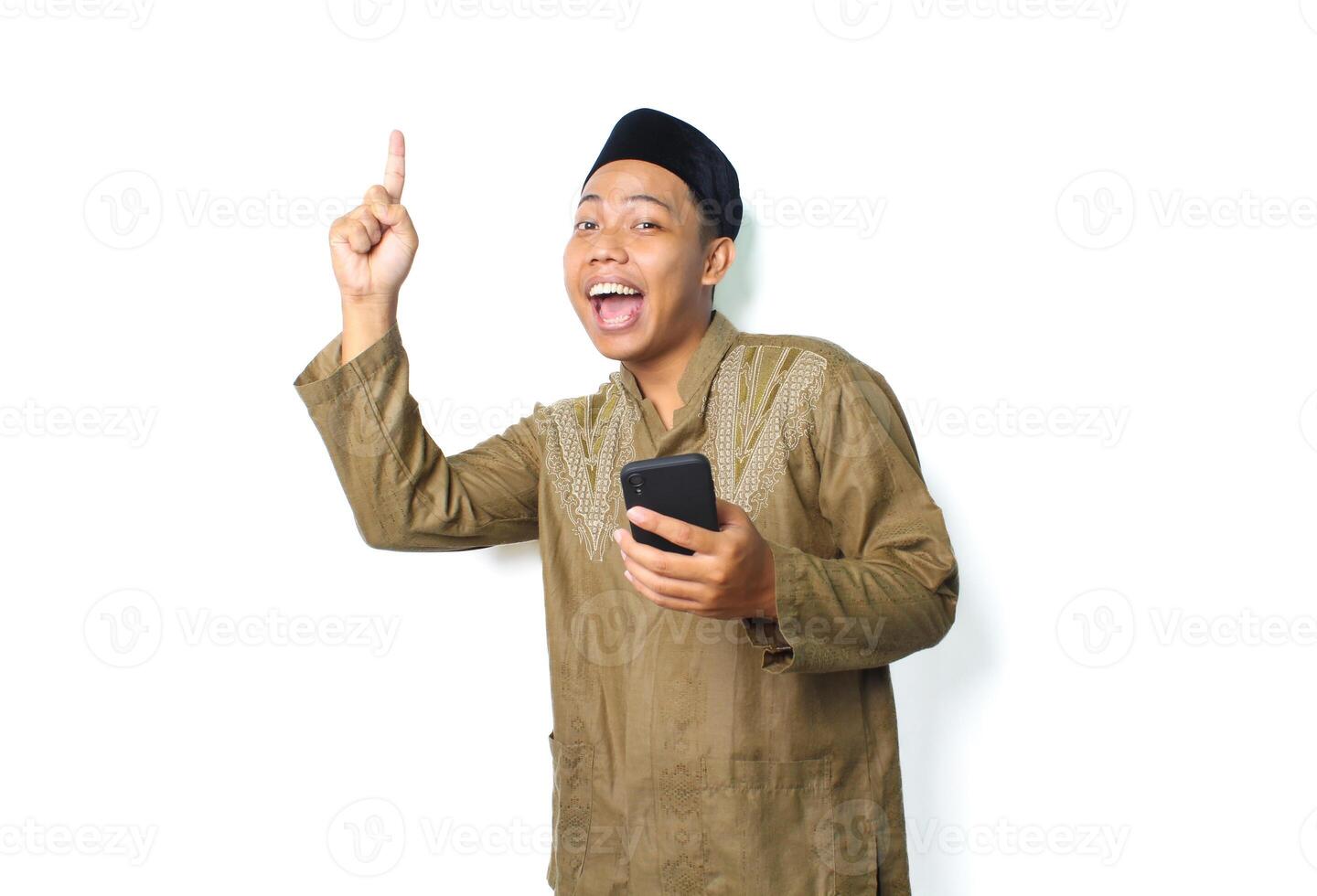 funny asian muslim man screaming while pointing to above with holding moblie phone isolated on white background photo