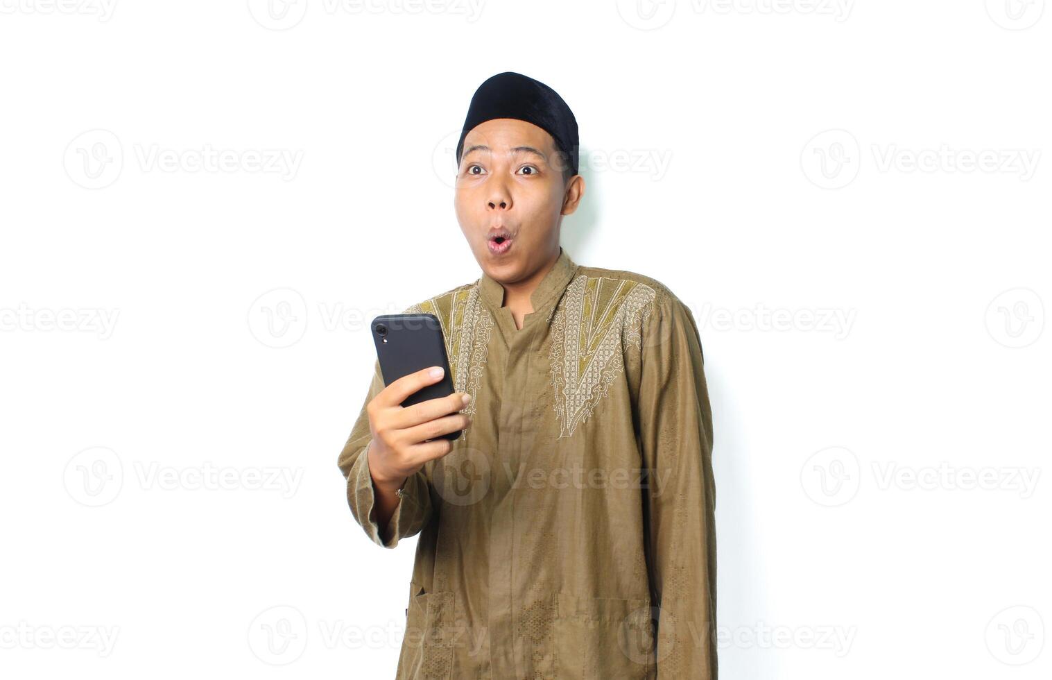 shocked asian muslim man wearing islamic dress holding mobile phone isolated on white background photo
