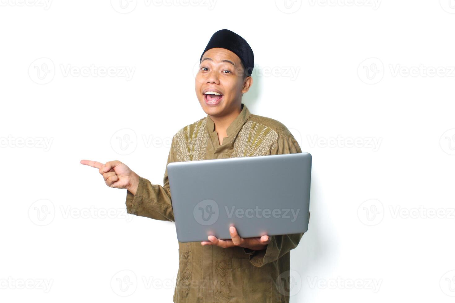 surprised asian muslim man pointing to beside with holding laptop isolated on white background photo