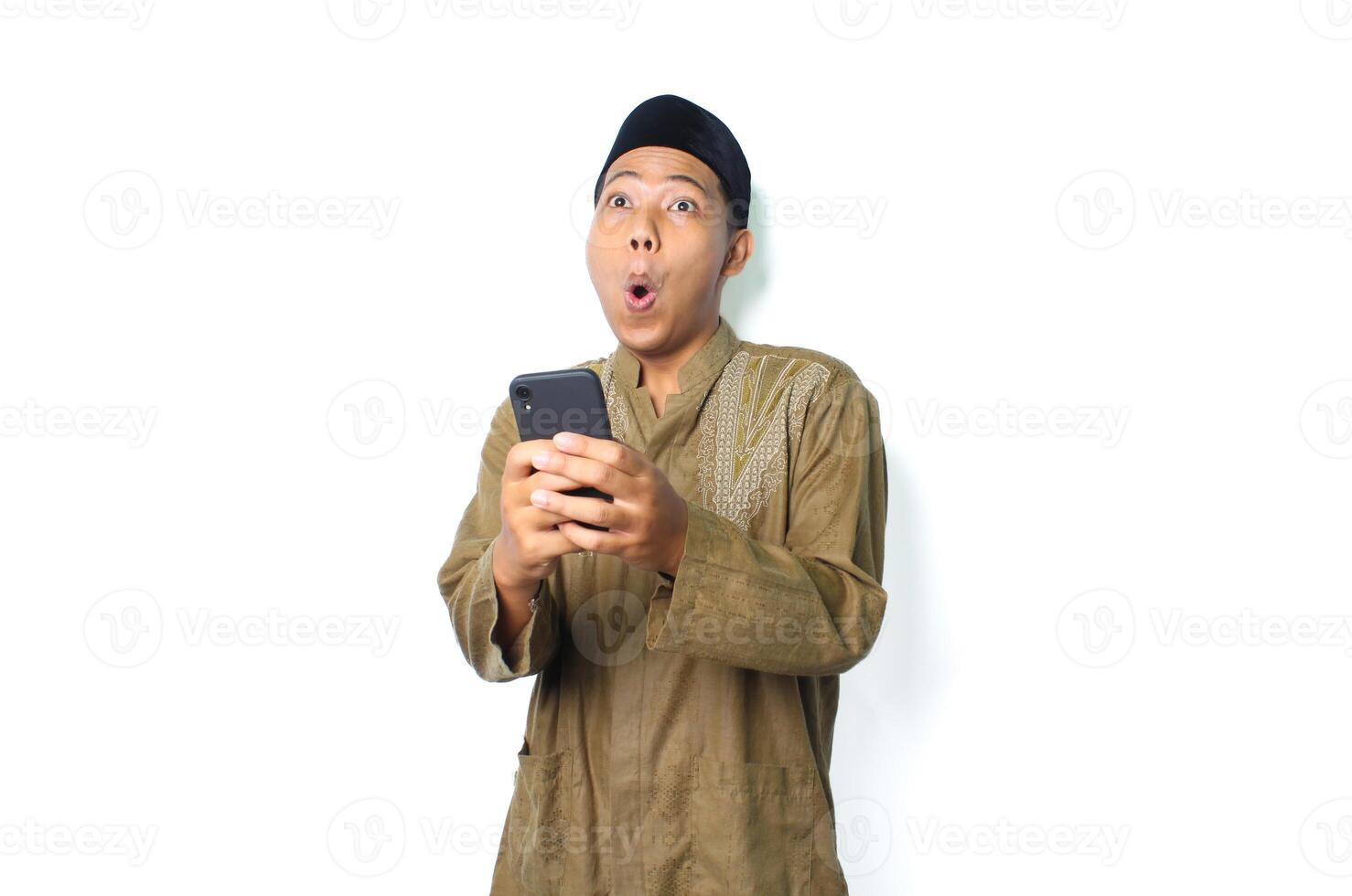 shocked asian muslim man wearing islamic dress holding mobile phone isolated on white background photo