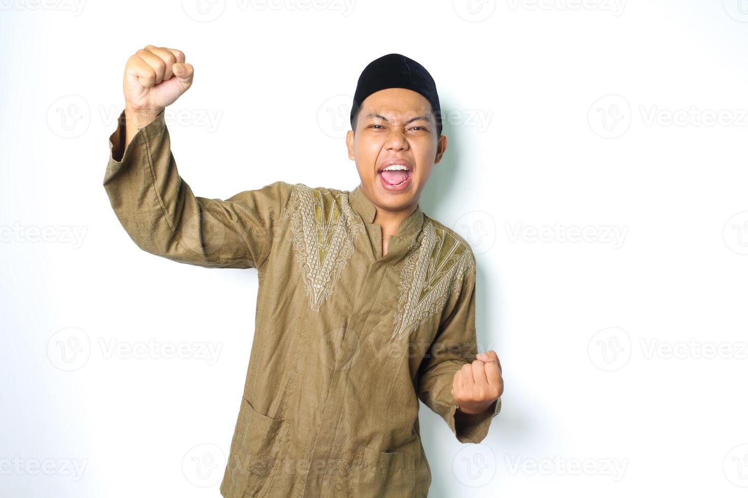 excited asian muslim man wearing islamic clothes raising fist showing victory gesture in eid mubarak celebration isolated on white gesture photo