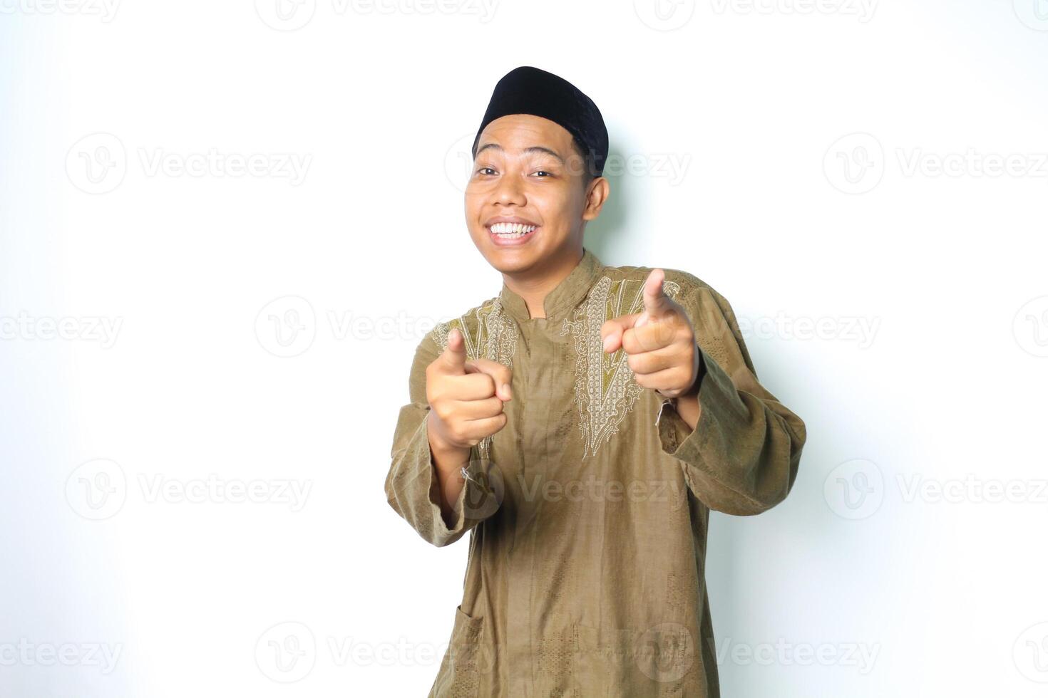 sonriente asiático musulmán hombre vistiendo koko ropa señalando a cámara con emoción aislado en blanco antecedentes foto