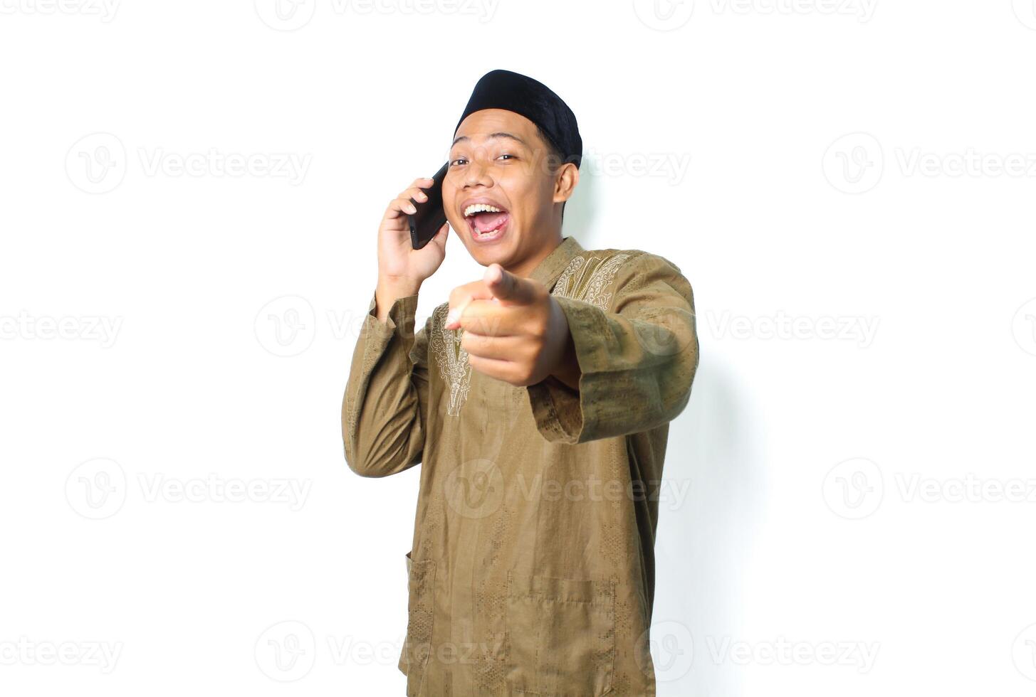 excited asian muslim male pointing at camera while talking using mobile phone isolated on white background photo