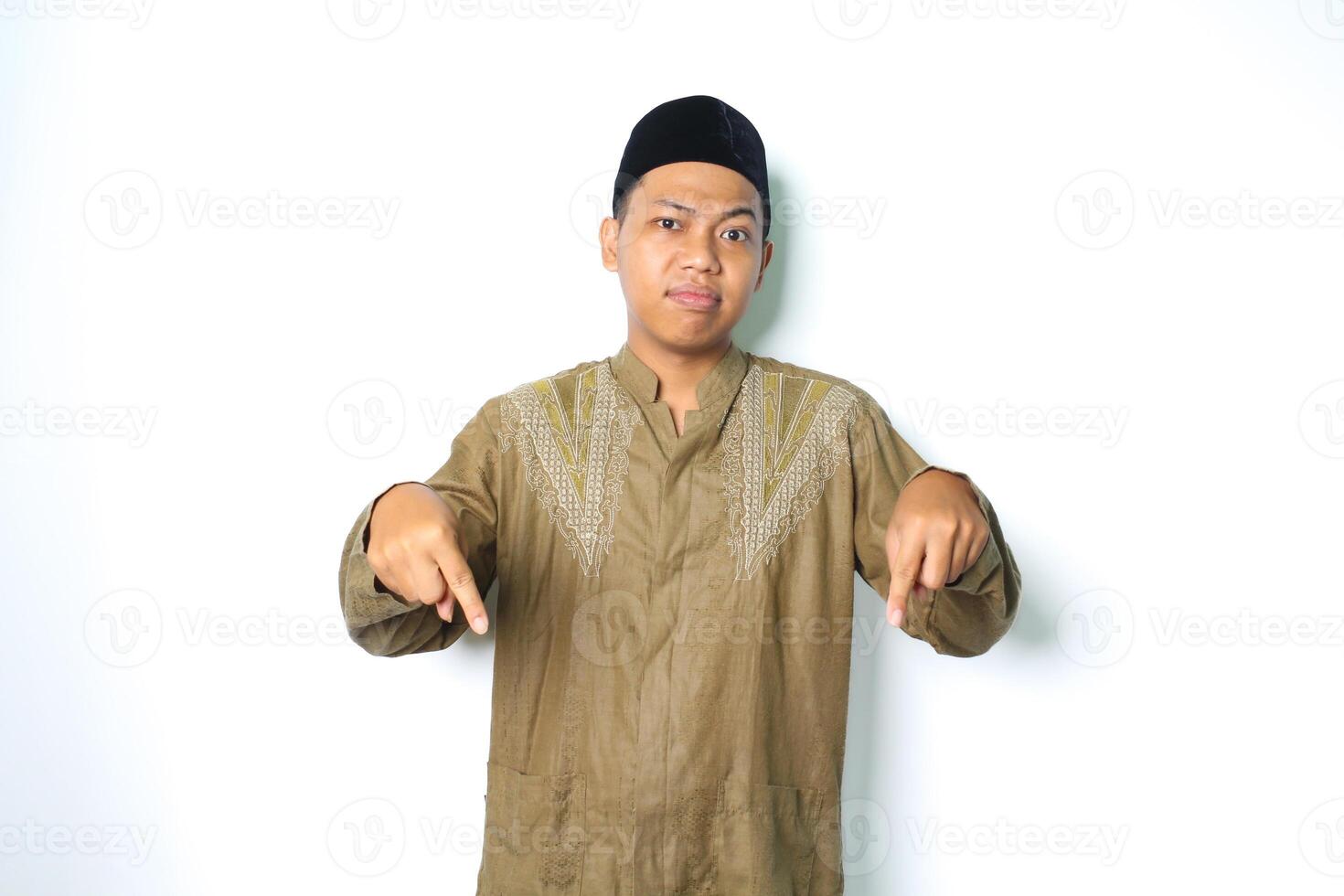 confuso asiático musulmán hombre vistiendo koko ropa señalando abajo con mirando a cámara aislado en blanco antecedentes foto
