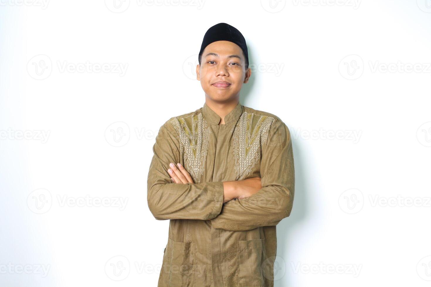 peaceful asian muslim man wearing islamic dress crossed arms and looking at camera standing over isolated white background photo