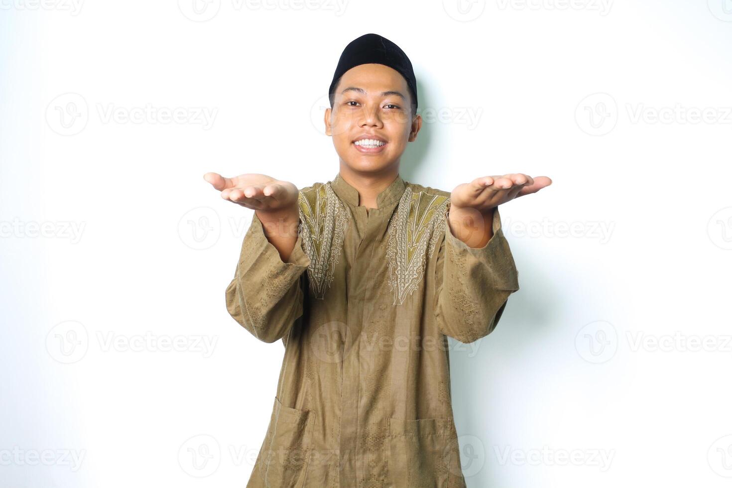 smiling asian muslim man wearing islamic dress presenting with open palm at camera isolated on white background photo
