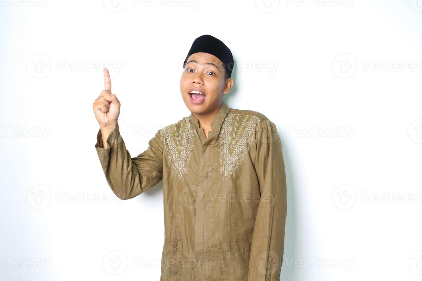 surprised asian muslim man wearing islamic clothes pointing to above isolated in white background photo