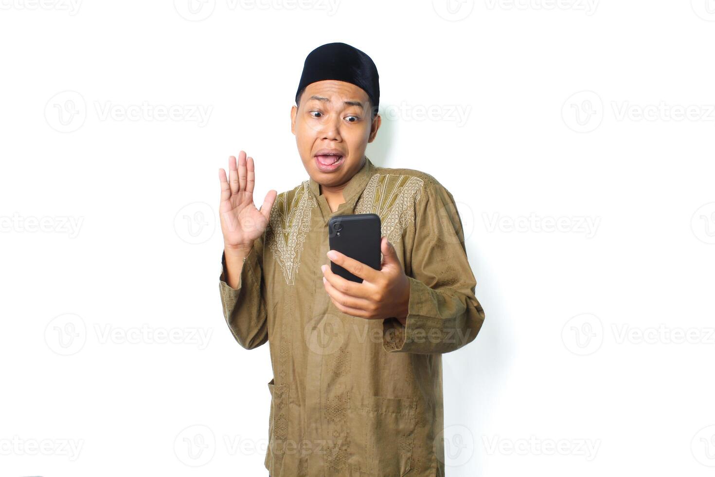asian muslim man holding mobile phone raising hand show shocked expression  isolated on white background photo