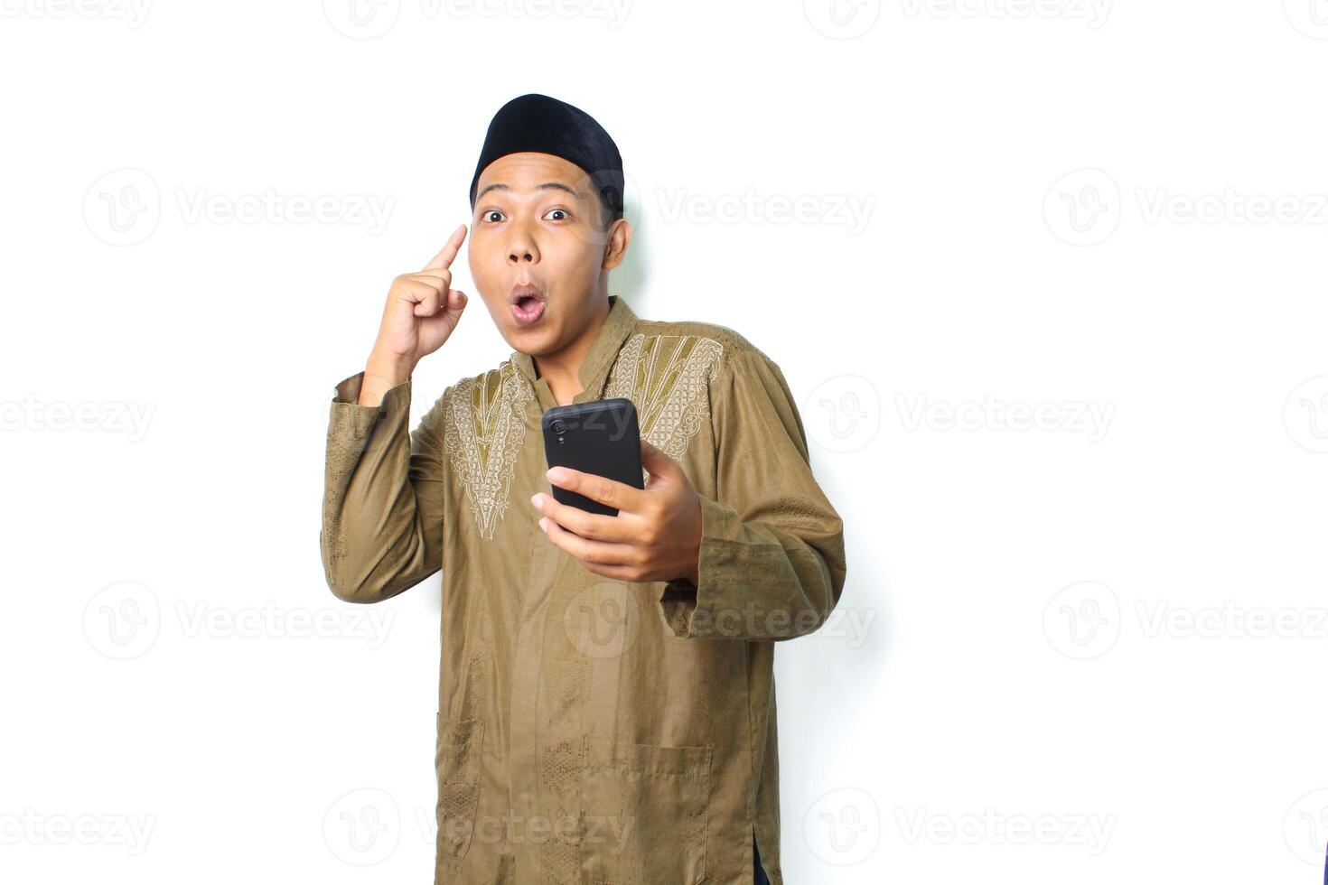 shocked asian muslim man holding mobile phone pointing to his head isolated on white background photo